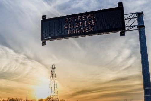 At sunset, a digital reader board over a roadway says "EXTREME WILDFIRE DANGER."