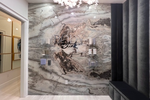 Entryway of Body by Blink with grey marble-esque wall, chandelier and 'Body by Blink' wall sign.