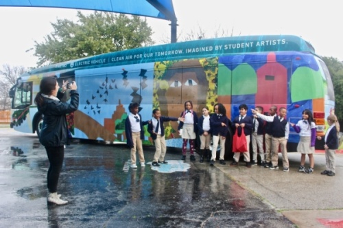 Students at Lee Lewis Campbell Elementary Media and Performing Arts Institute in East Austin point to their classmate holding the red bag, whose artwork is featured on the new electric bus. (Amy Denney/Community Impact Newspaper)