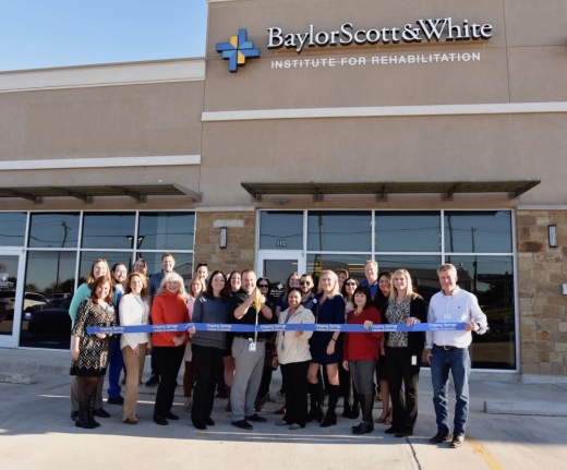 A photo of a group of people holding a ribbon, with one man getting ready to cut it with scissors, in front of a Baylor Scott & White Institute for Rehabilitation location.