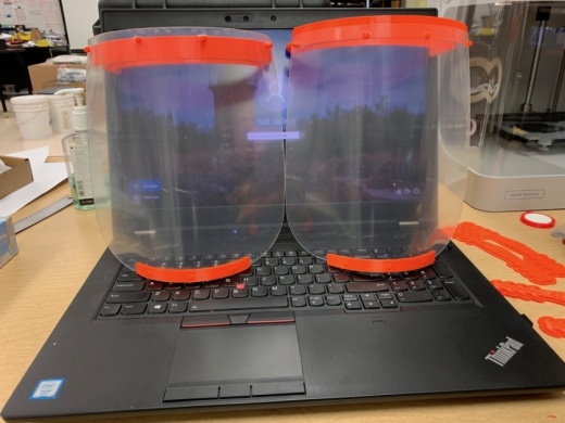 A photo of two clear face shields sitting atop a black laptop computer