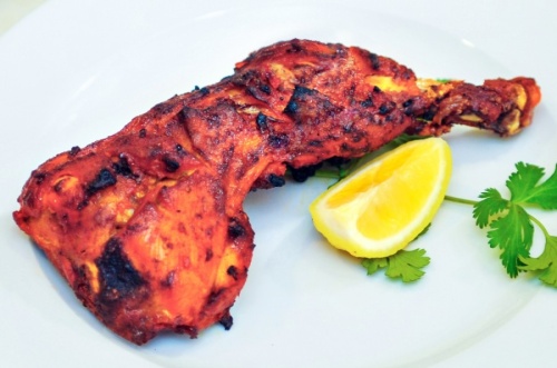 Tandoori chicken with a lemon slice and stem of cilantro, served on a plate