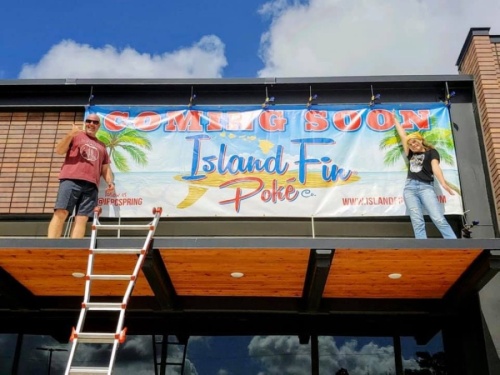Franchise co-owner Matt Gustafson (left) and his daughter hang the "coming soon" sign for their new Island Fin Poke Co. location in Spring. (Courtesy Matt Gustafson)