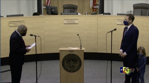 Screen shot of two men and a little girl in the Travis County Commissioners Court chambers