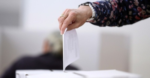 Photo of a hand dropping a ballot in a box