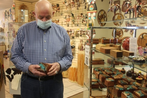 Turquoise Trading Post owner Jim Williamson looks at a handmade wooden box set with turquoise. (Olivia Aldridge/Community Impact Newspaper)