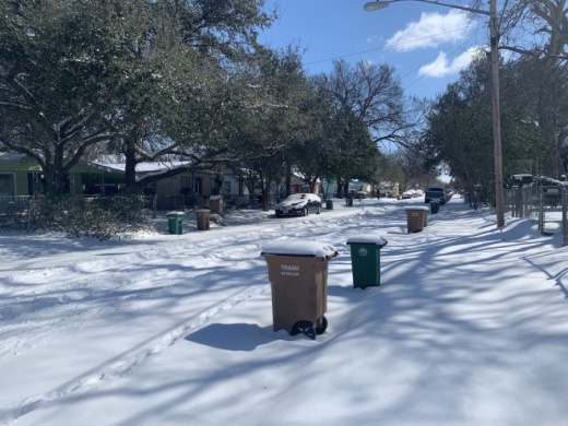 Photo of a street and trash bins covered in snow