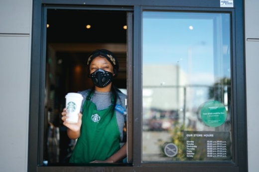 Starbucks employee standing at a drive-thru window, holding a drink