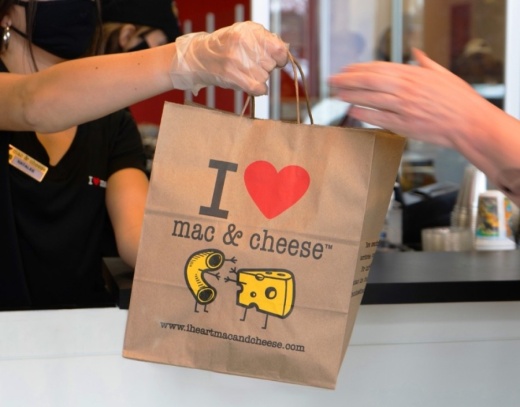 A restaurant worker handing an I Heart Mac & Cheese bag to a customer
