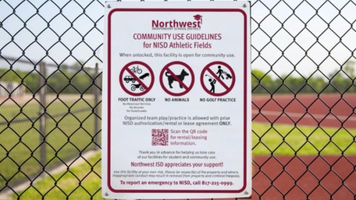 A community use guidelines sign on a fence near an athletic track