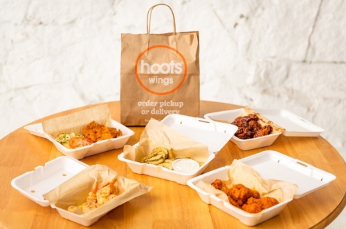 Take-out containers of food on a table surrounding a Hoots Wings bag
