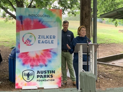 Photo of a woman at a podium and a tie dye sign reading "Zilker Eagle"