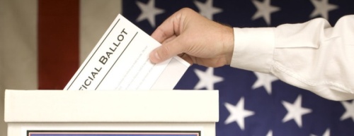 A hand depositing a ballot into a ballot box.