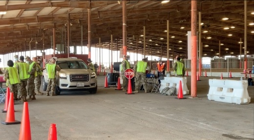 A car surrounded by people dressed in camouflage and bright yellow vests.
