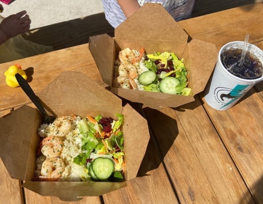 Cardboard to-go boxes of shrimp with rice and salad, on a table next to a cup of soda and a rubber duck