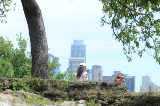Photo of a woman and girl walking the trail with the Austin skyline behind them