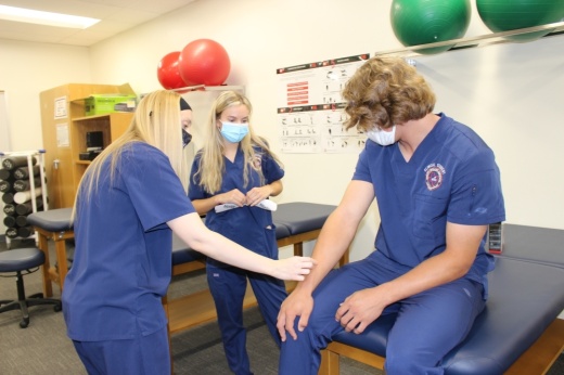 McKinney North High School CTE department chair Aly Deal (left) shows student Katie Gimlin how to apply kinesiology tape on fellow student Ethan Weslowki. (Miranda Jaimes/Community Impact Newspaper)