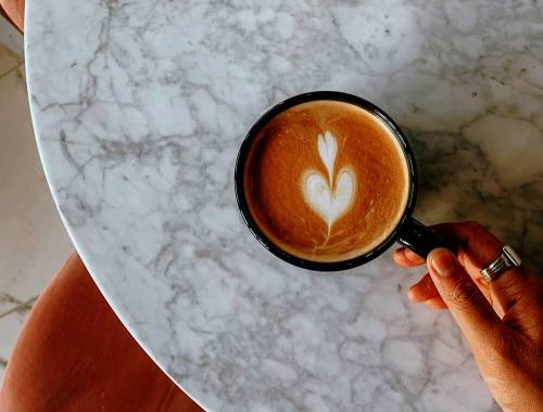 A woman wearing rings holds a coffee cup on a marble counter