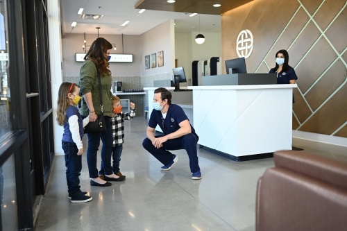 A health care worker greeting a mother and two kids in an urgent care lobby
