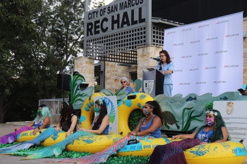 Mayor Jane Hughson speaking at the kick off event, surrounded by mermaids. (Zara Flores/Community Impact Newspaper).