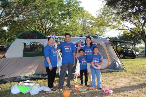 family of five in matching blue t-shirts standing outside by grey tents