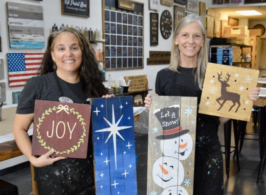 Studio manager Rochelle Tramel (left) and studio owner Jan Scriven hold Christmas-themed projects. (Photos by Taylor Girtman/Community Impact Newspaper)