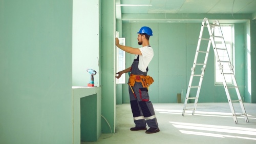 Worker installs plasterboard drywall at a construction site