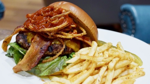 This dish has a premium beef patty served on a brioche bun with bacon, cheddar cheese, onion strings, house-made BBQ sauce, lettuce and tomato and comes with seasoned house fries. (Amber Friend/Community Impact Newspaper)