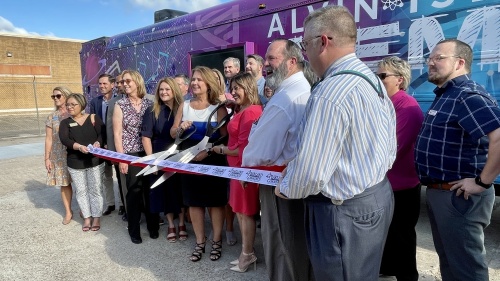 Alvin ISD Superintendent Carol Nelson (white and blue dress) and Ana Pasarella, the district's director of family and community engagement, hold the ceremonial scissors for the ribbon cutting of the STEM Explorer Bus. (Andy Yanez/Community Impact Newspaper)