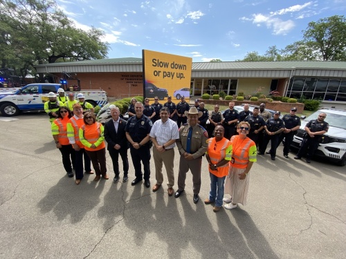 TxDOT employees stand in front of a sign that reads "Slow down or pay up."