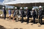 Eight people hold shovels full of sand with hard hats