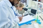 Stock image of a man writing on a clipboard while a woman looks in a microscope.