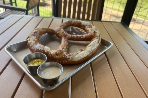 A large, salted soft pretzel is served with gouda cheese sauce and mustard for the Big as Your Face Pretzel (0). (Maegan Kirby/Community Impact Newspaper)