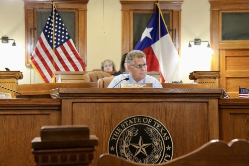 County Judge sits on the dias with the Texas flag behind him