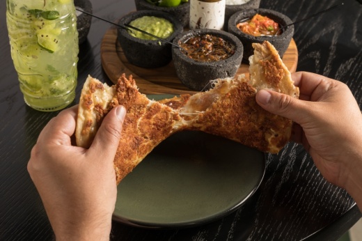 Two hands holding a quesadilla over a plate. 