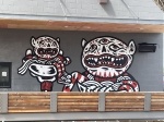 Grey building with monster-like murals painted on the front in red and white paint. 