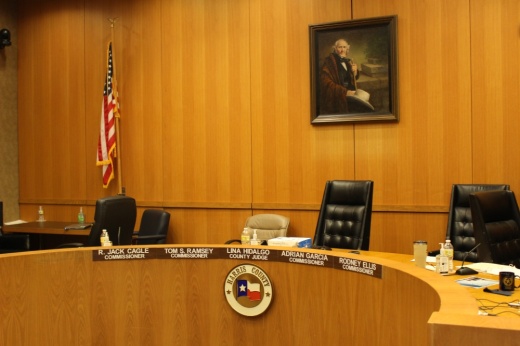 This depicts empty seats in an orange courtroom with the nameplates of the commissioners in front of the seats.