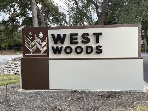 Brown and white sign that says West Woods. 