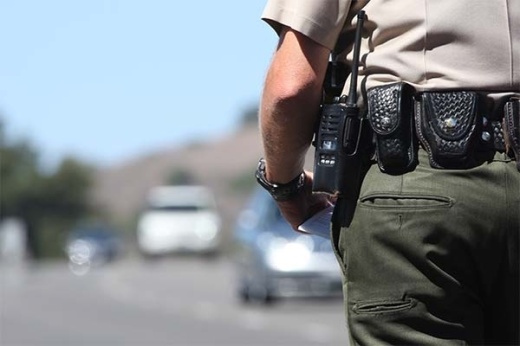 This is a close-up focused on the belt of a police officer with cars driving on a road in the background.