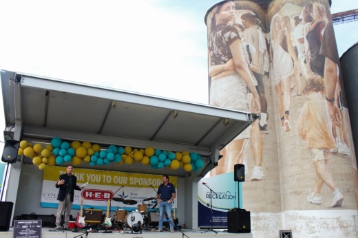 City Manager Paul Grimes and Mayor George Fuller speak on a stage in front of a mural on silos.