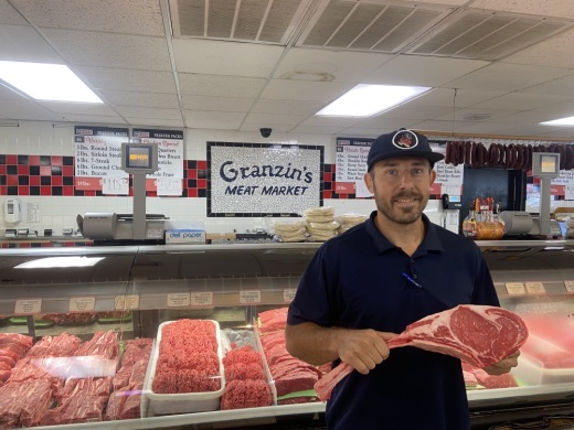 Co-owner Zane Granzin holds a tomahawk steak at Granzin's Meat Market. (Photos by Christopher Green/Community Impact Newspaper)