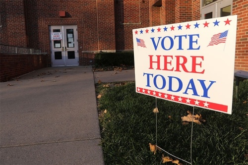 A red, white and blue sign reading "Vote Here Today" mounted in front of a brick building