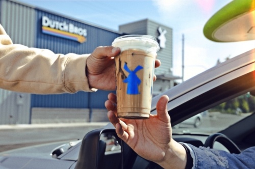Hand-off of a Dutch Bros coffee with the building and logo in the background