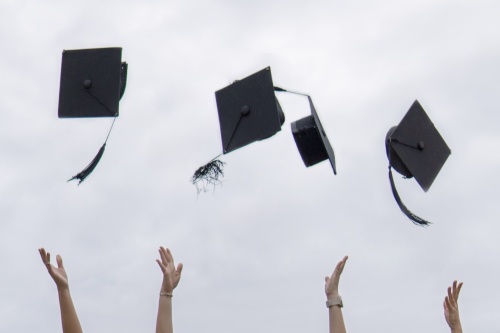 Four black graduation caps being thrown in the air.