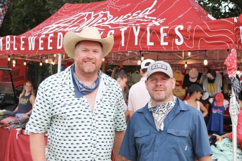 two founders of tumbleweed texstyles standing in front of booth full of their shirts