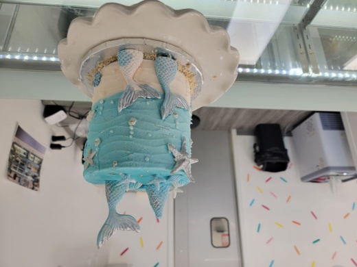 A mermaid-themed cake design on display at the counter of Cakes U Crave Dessert Bar.