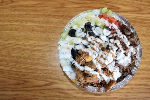 The combo chicken and lamb gyro platter ($10.99) is served with rice, lettuce, tomato, onion, cucumber, corn, black olives, jalapeno, pickled vegetables, chickpeas and sliced pickles. It is topped with signature white sauce and hot sauce. (Karen Chaney/Community Impact Newspaper)
