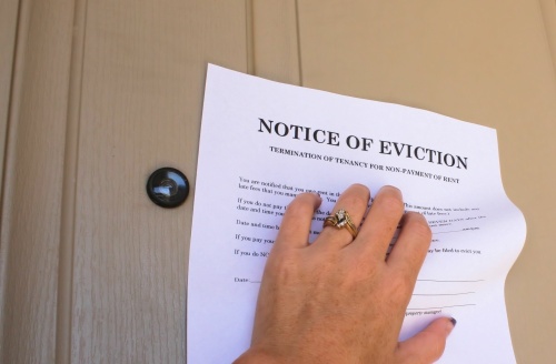 This is a picture of a hand holding up a paper that says "notice of eviction" against a door.