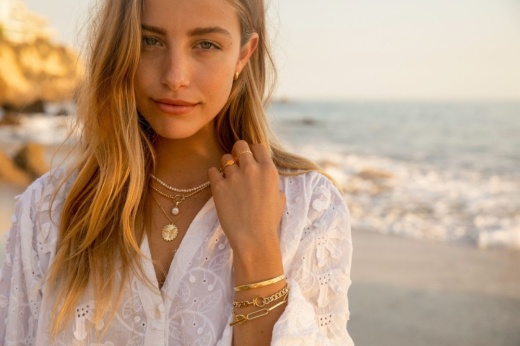 woman wearing a white shirt and several jewelry pieces on a beach