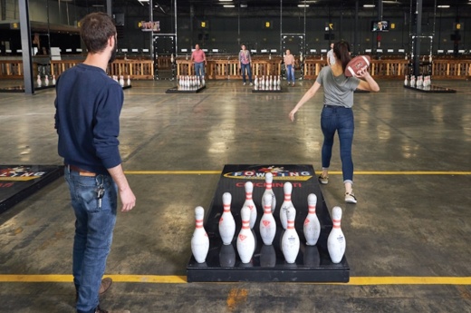 woman throwing football at bowling pins